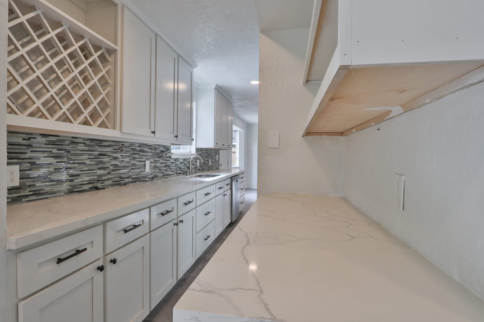 Galley kitchen with white cabinets, long countertop and mosaic backsplash